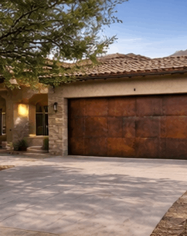 Rustic metal garage door with an oxidized steel finish on a tan stucco home